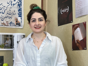 Yasaman Baghban seated on her desk, surrounded by images pinned to the walls.